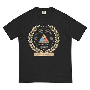 Puede incluir: Camiseta negra con un emblema dorado y blanco de la 2ª División Acorazada. El emblema incluye texto como "United States Army", "2nd Armored Division", "Cold War Veteran" y "Hell on Wheels". La camiseta es de ajuste cómodo.
