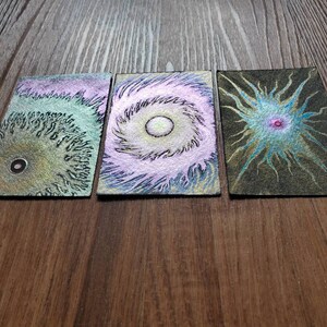 May include: Three small, rectangular cards with abstract, colorful, swirling designs. Each card has a central circle with a different color and pattern.