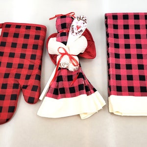 May include: A set of three kitchen towels in a red and black buffalo check pattern. The towels are bundled together with a red ribbon and a wooden spoon with the text "Bless with Love" on it.