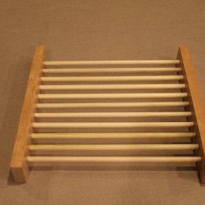 May include: A wooden dish rack with a rectangular frame and multiple horizontal dowels. The rack is made of light-colored wood and is designed to hold dishes for drying. The design is simple and functional.