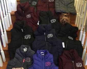 Puede incluir: Una colección de 14 chalecos acolchados en varios colores, incluyendo azul marino, burdeos, negro, gris y beige. Cada chaleco presenta un monograma bordado diferente en la parte delantera.