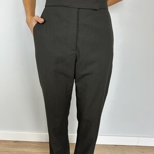 Puede incluir: Pantalones de color carb&oacute;n oscuro con una cintura ancha y un dise&ntilde;o de pierna recta. Los pantalones tienen bolsillos delanteros y un ajuste a medida. La tela parece ser un material liso y tejido, adecuado para un look profesional y pulido.