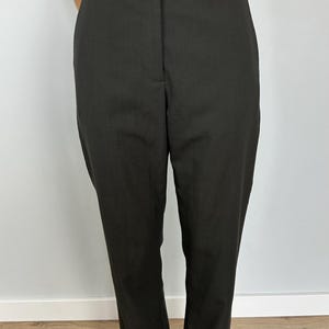 Peut inclure: Pantalon noir avec une large ceinture et une coupe droite. Le pantalon a un design classique avec une coupe ajustée. Le tissu semble être de couleur foncée unie, adapté à diverses occasions.