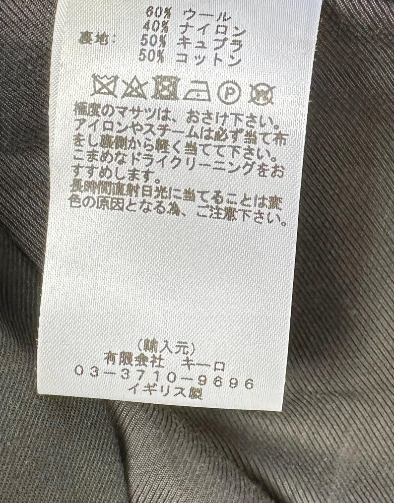Puede incluir: Una etiqueta de ropa blanca con texto japon&eacute;s y s&iacute;mbolos de cuidado. Indica la composici&oacute;n de la tela: 60% lana, 40% nailon, y forro de 50% cupro y 50% algod&oacute;n. Incluye instrucciones de lavado y datos del fabricante.