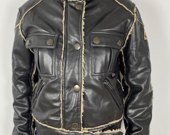 May include: A brown faux leather jacket with a shearling lining and frayed edges. The jacket has a zipper closure, a stand-up collar, and two flap pockets.