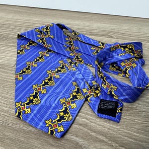 以下が含まれることがあります： 金色と黒色の模様が施された青いシルクネクタイ。ネクタイには、青と黒のラベルが付いており、「ドライクリーニング不可、石油系ドライクリーニングのみ、イタリア製」と記載されています。