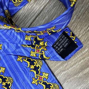 以下が含まれることがあります： 金色と黒の模様が施された青いシルクネクタイ。ネクタイには、「ドライクリーニングのみ、石油系溶剤は使用しないでください、漂白しないでください、低温でアイロンをかけてください。」というケアラベルが付いています。