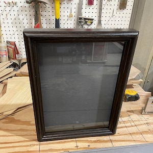 May include: A dark brown wooden shadow box with a clear glass front. The shadow box is empty and ready to display your favorite items.