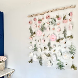 May include: A wall decor piece featuring a branch with pink and white artificial flowers and greenery. The flowers are arranged in a cascading pattern, creating a romantic and whimsical look.