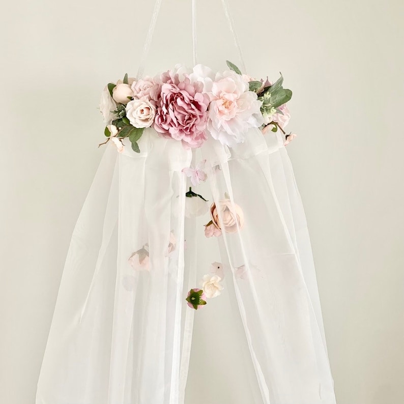 May include: A white canopy with a pink and white floral garland hanging from the top. The garland is made of artificial flowers and greenery.