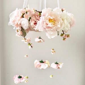 May include: A pink and white floral mobile with a ring of flowers and hanging blossoms. The mobile is made of silk flowers and is perfect for a nursery or child's room.