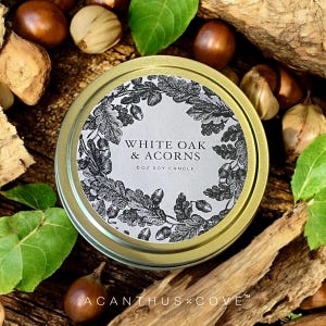 May include: A gold tin candle with a white label that says "White Oak & Acorns" and "6 oz Soy Candle". The label features a black and white illustration of oak leaves and acorns.