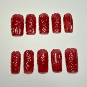 May include: Ten red, rectangular, carved objects are arranged in two rows. Each object has a unique design, including vertical lines, geometric patterns, and swirling textures. The objects appear to be made of a translucent material.