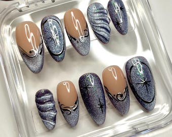 Könnte beinhalten: Ein Set aus zehn mandelförmigen Press-on-Nägeln mit nudefarbener Basis und silbernen Cat-Eye-Glitzerspitzen. Das Design umfasst handgemalte schwarze Sternakzente, geschwungene Linien und zwei Nägel mit einer erhabenen, texturierten 3D-Wellenstruktur.
