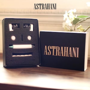 以下が含まれることがあります： 蓋に金色の文字でASTRAHANIと印刷された黒い長方形のギフトボックス。開いた箱の中には、黒いフォームインサートがあり、白いペン、2つの小さな白い円形の物体、および白い歯のようなコンポーネントが固定されています。