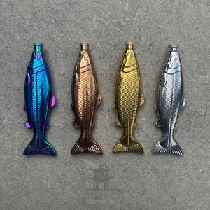 May include: Four fish-shaped bottle stoppers in iridescent blue, bronze, gold, and silver. Each stopper has a detailed scale pattern and a small, cylindrical top. The fish are arranged in a row on a gray surface.