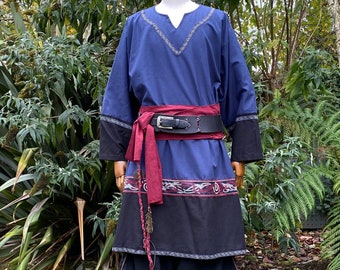 May include: A blue tunic with a red sash and black belt. The tunic has a decorative pattern around the bottom hem and a V-neck. The sash is tied at the waist and the belt has a silver buckle.