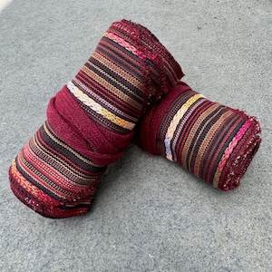 May include: Two rolled up pieces of fabric with a striped pattern in shades of red, brown, black, and white. The fabric is tied together with a burgundy cord.