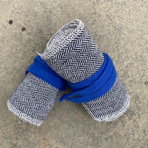 May include: Two rolled up pieces of fabric with a herringbone pattern in black and white. The fabric is tied together with a blue ribbon.