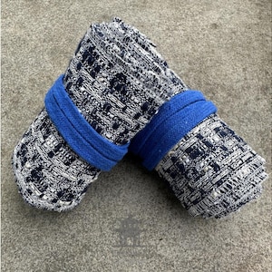 May include: Two rolled up bath mats with a blue trim. The mats are black and white with a woven pattern.