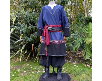 May include: A long blue tunic with a red sash and black trim. The tunic has a black and gray patterned bottom and a silver belt with a buckle. The tunic is worn over black pants and black boots.