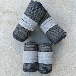 May include: Four black and grey fabric rolls with a herringbone pattern. Each roll is wrapped with a grey band.