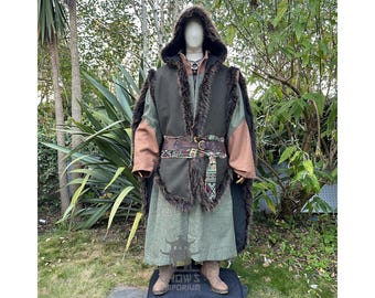 May include: A hooded cloak and vest ensemble with faux fur trim, brown leather belt, and a long green tunic. The outfit features brown and green color blocking on the sleeves and vest. The mannequin is wearing a necklace and boots.