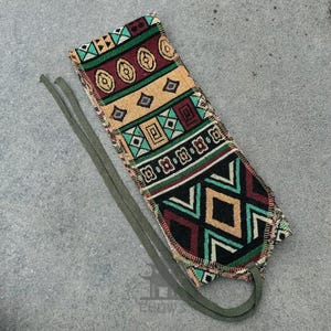 May include: A colourful patterned fabric pouch with a green, red and yellow geometric design. The pouch has a drawstring closure and a long green cord.