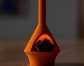 May include: An orange, mid-century modern style fireplace sculpture. The sculpture has a triangular opening with a glowing orange light inside, and contains dark, square-shaped objects. The fireplace is set on a wooden surface.