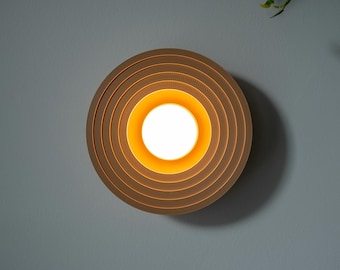 Può includere: Un apparecchio di illuminazione a soffitto circolare con un design a strati. La luce è in legno e ha un bagliore caldo e giallo.