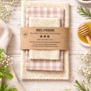 May include: A set of reusable beeswax food wraps in various sizes, featuring a floral and gingham pattern in cream and pink. The wraps are made of cotton infused with beeswax, pine resin, and jojoba oil. The package includes three wraps with dimensions of 8x8, 12x12, and 15x15 inches.