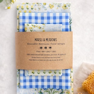 May include: A set of reusable beeswax food wraps from Marsli & Meadows. The wraps are made of 100% cotton and come in various sizes, including 8x8, 12x12, and 15x15 inches. The wraps feature floral and blue gingham patterns.