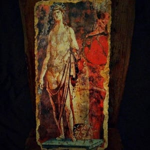 May include: A rectangular, aged painting depicting a classical figure with a laurel wreath, draped in fabric. The artwork features a red shield and a column against a backdrop of red and yellow hues. The edges are rough, suggesting age.