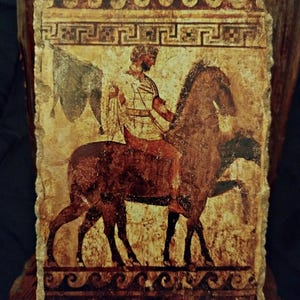 May include: A rectangular, aged stone carving depicting a figure on horseback. The rider, in a tunic, holds a cloth. The horse is brown, and the background is a faded beige. Decorative borders with wave and geometric patterns frame the image.