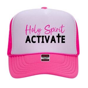 May include: A white and pink trucker hat with the text "Holy Spirit Activate" in black and pink lettering. The hat has a mesh back and a pink brim.