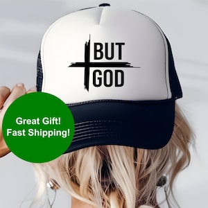 May include: A black and white trucker hat with a black cross and the text "BUT GOD" on the front. The hat is worn by a person with blonde hair.