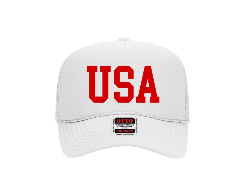 May include: White trucker hat with the red letters "USA" across the front. The hat has a mesh back and a curved brim. A small tag with text is visible on the front.