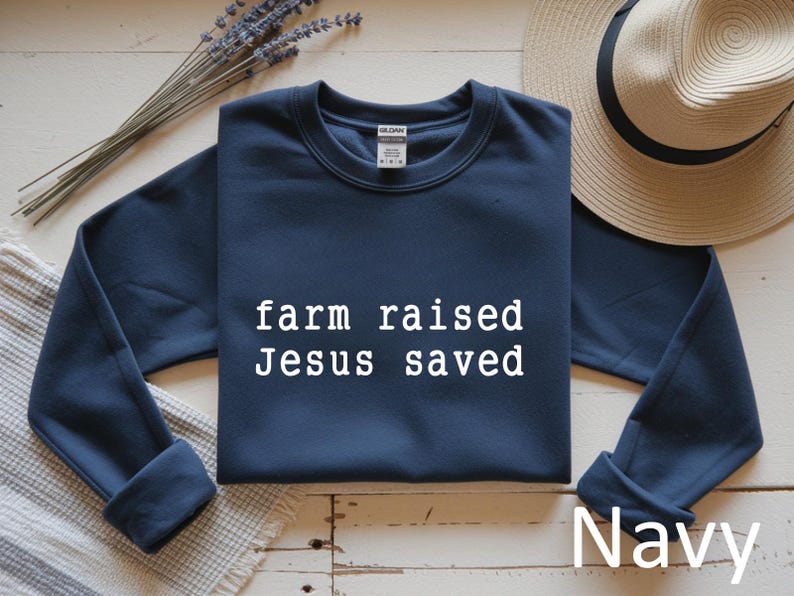 May include: Navy blue sweatshirt with the text "farm raised Jesus saved" in white. A straw hat and lavender sprigs are in the background. The word "Navy" is also visible.