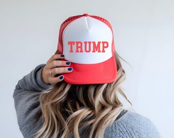 May include: A red and white trucker hat with a white mesh back. The front of the hat has the word "TRUMP" printed in red.