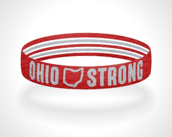 May include: A red fabric wristband featuring white horizontal stripes along the top and bottom edges. The text OHIO STRONG is printed in white capital letters on the front, with a white outline of the state of Ohio between the two words.