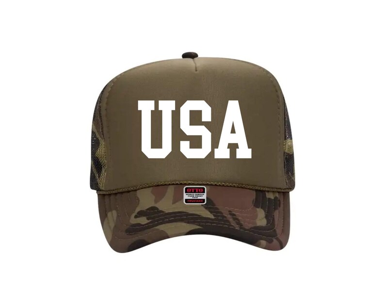 May include: A trucker hat with a camouflage brim and a khaki-colored crown. The word "USA" is printed in bold white letters on the front. The hat has a mesh back and a small tag on the brim.