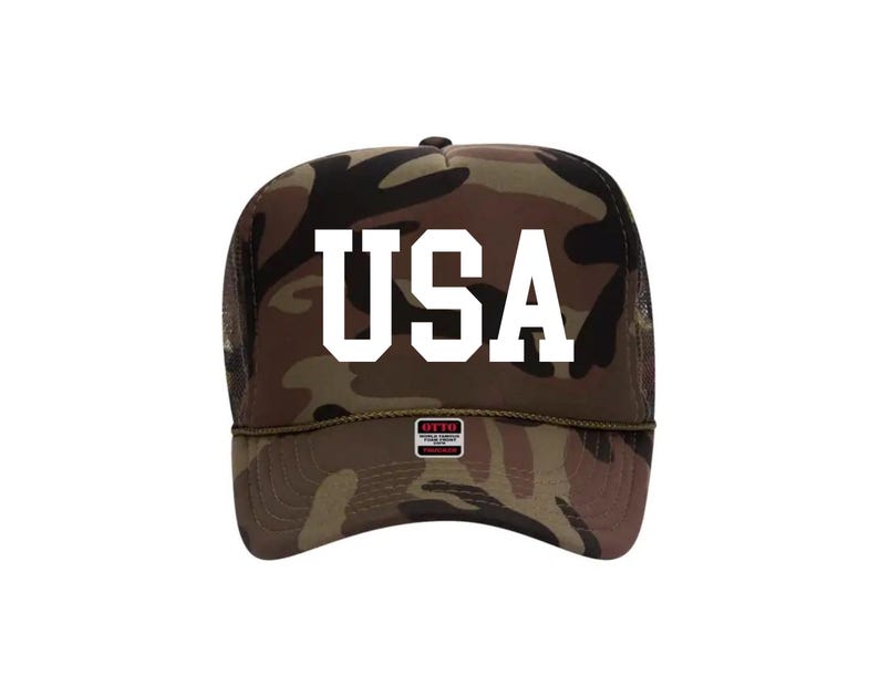 May include: Camouflage trucker hat with the word "USA" in bold white letters. The hat features a mesh back and a curved brim. The hat has a small tag that says "OTTO".