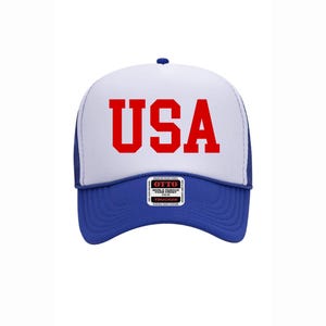 May include: A blue and white trucker hat with the word "USA" in red block letters across the front. The hat has a blue brim and a white foam front. The hat also has a small patch that says "OTTO".