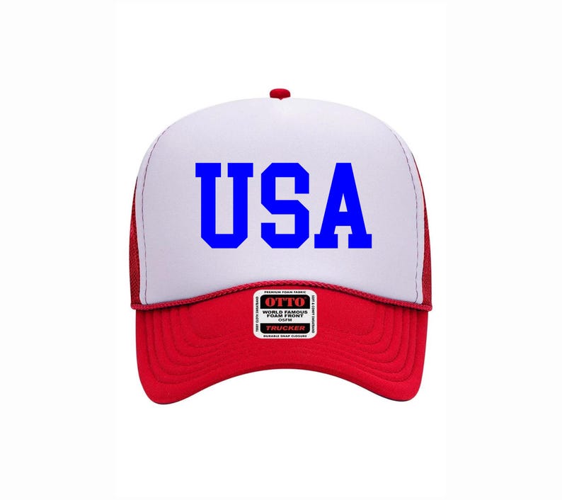 May include: A red, white, and blue trucker hat with the word "USA" in bold blue letters across the front. The hat features a white foam front, a red brim, and a red mesh back. A small label is visible on the front.