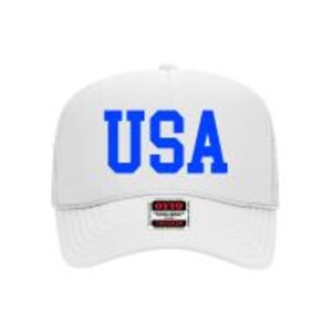 May include: White trucker hat with the word "USA" in blue block letters across the front. The hat has a structured front panel and a mesh back. A small tag is visible on the brim.