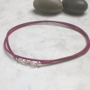 May include: A double-strand leather cord necklace in a deep purple color with a silver clasp and two silver beads.