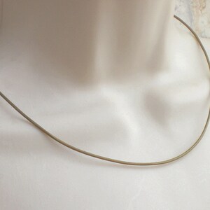 May include: A simple, thin, gold-colored necklace. The necklace is made of a single, continuous piece of metal and has a smooth, polished finish.