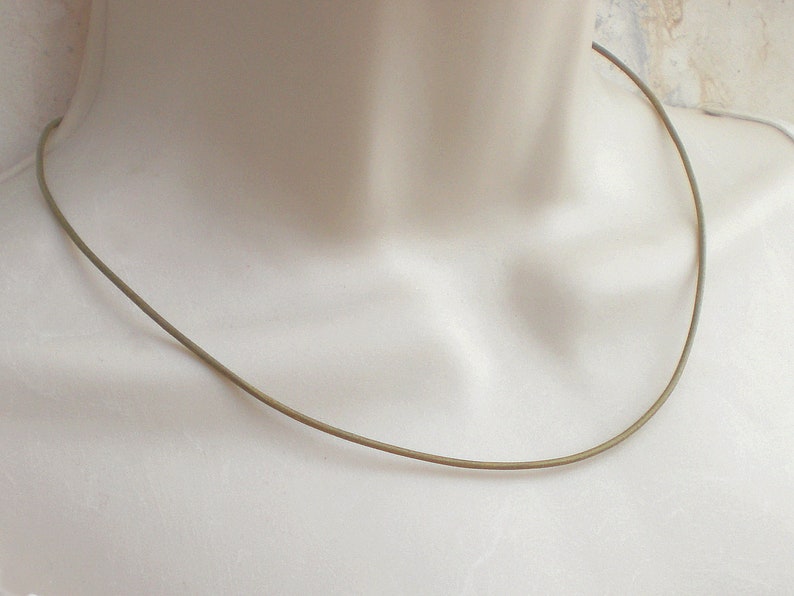 May include: A simple, thin, gold-colored necklace. The necklace is made of a single, continuous piece of metal and has a smooth, polished finish.