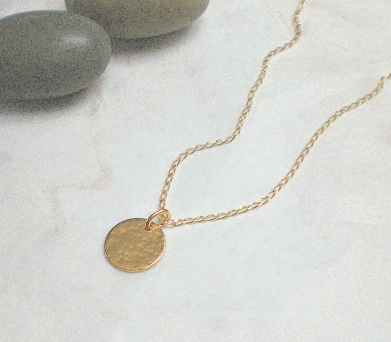May include: A gold chain necklace with a hammered gold circle pendant.