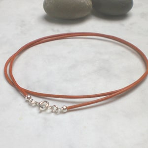 May include: A brown leather cord necklace with a silver clasp. The cord is about 18 inches long.